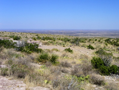 [The ground, covered in scrubgrass and cacti, seems flat for as far as the eye can see. Two picnic tables with benches and a grill are on some gravel amid the brushy vegetation.]